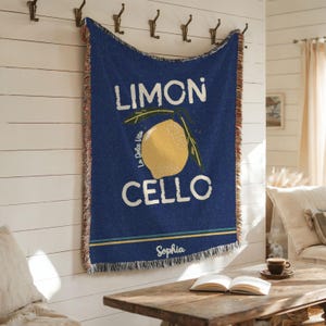May include: A blue woven throw blanket with a lemon illustration and the text "Limon Cello" and "La Dolce Vita". The blanket has a fringe border and the name "Sophia" is written at the bottom.