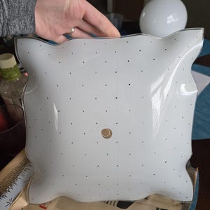 May include: White ceiling light fixture with a wavy edge and a pattern of small holes. The fixture has a central hole for the light bulb.