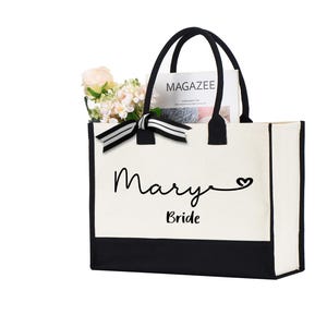 May include: White canvas tote bag with black trim and handles. The bag has a black ribbon with white stripes and the text "Mary Bride" with a heart symbol.