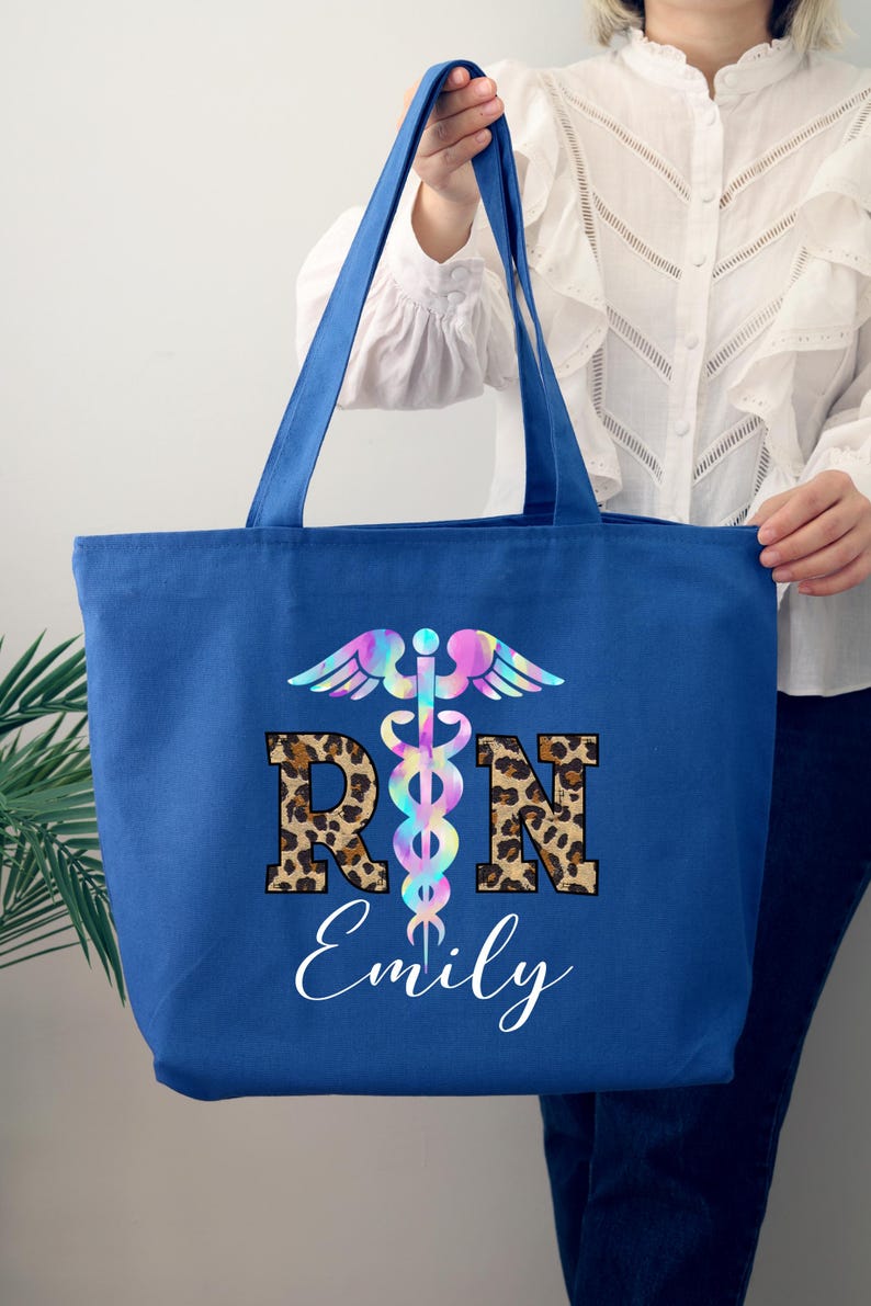 May include: A blue canvas tote bag with a rainbow-colored medical symbol and the letters "RN" in leopard print. The name "Emily" is written below the letters.