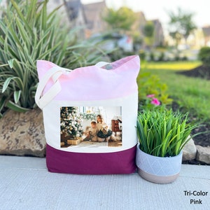 May include: A tri-color tote bag with a pink, white, and burgundy design. The bag features a photo of a family with a dog in front of a Christmas tree.