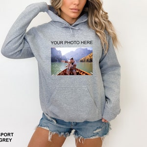 May include: A gray hooded sweatshirt with a pocket on the front. The sweatshirt has a photo of a couple on a boat on a lake printed on the front. The text "YOUR PHOTO HERE" is printed above the photo.