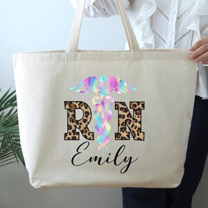 May include: A white canvas tote bag with a rainbow-colored medical symbol and the letters "RN" in a leopard print design. The name "Emily" is printed below the letters.