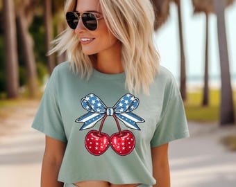 May include: A light green crop top featuring a patriotic cherry design. The cherries are red with white stars, and the bow is blue with white stars. The shirt is a casual style.