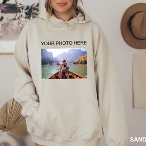 May include: A beige hoodie with a large pocket on the front. The hoodie has the text "YOUR PHOTO HERE" printed on the front, and a photo of two people in a boat on a lake is printed below the text.