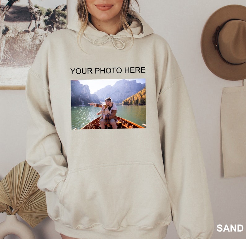 May include: A beige hoodie with a large pocket on the front. The hoodie has the text "YOUR PHOTO HERE" printed on the front, and a photo of two people in a boat on a lake is printed below the text.