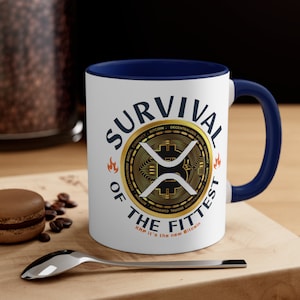 Pode incluir: Caneca de cerâmica branca com borda e alça azuis. A caneca apresenta um círculo dourado com um logotipo XRP branco e o texto "Survival of the Fittest" com as palavras "XRP it's the new Bitcoin" na parte inferior.