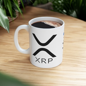 Pode incluir: Caneca de cerâmica branca com um logotipo XRP preto e a palavra "XRP" impressa na frente. A caneca está cheia de café.