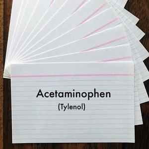 May include: A stack of white index cards with pink and blue lines. The top card has the text "Acetaminophen (Tylenol)" written in black.