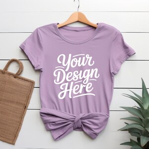 K&ouml;nnte beinhalten: Ein lavendelfarbenes T-Shirt mit kurzen &Auml;rmeln und Rundhalsausschnitt. Das Shirt ist unten verknotet und hat den Text "Your Design Here" in wei&szlig; auf der Vorderseite.