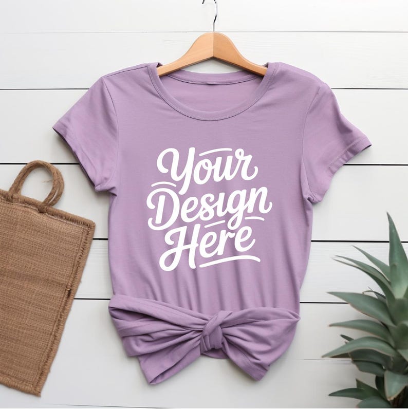 K&ouml;nnte beinhalten: Ein lavendelfarbenes T-Shirt mit kurzen &Auml;rmeln und Rundhalsausschnitt. Das Shirt ist unten verknotet und hat den Text "Your Design Here" in wei&szlig; auf der Vorderseite.