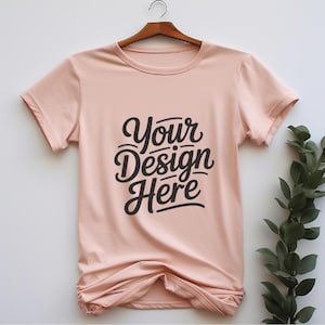 K&ouml;nnte beinhalten: Ein hellrosa T-Shirt mit kurzen &Auml;rmeln und Rundhalsausschnitt. Das Shirt hat den Text "Your Design Here" in Schwarz auf der Vorderseite aufgedruckt.