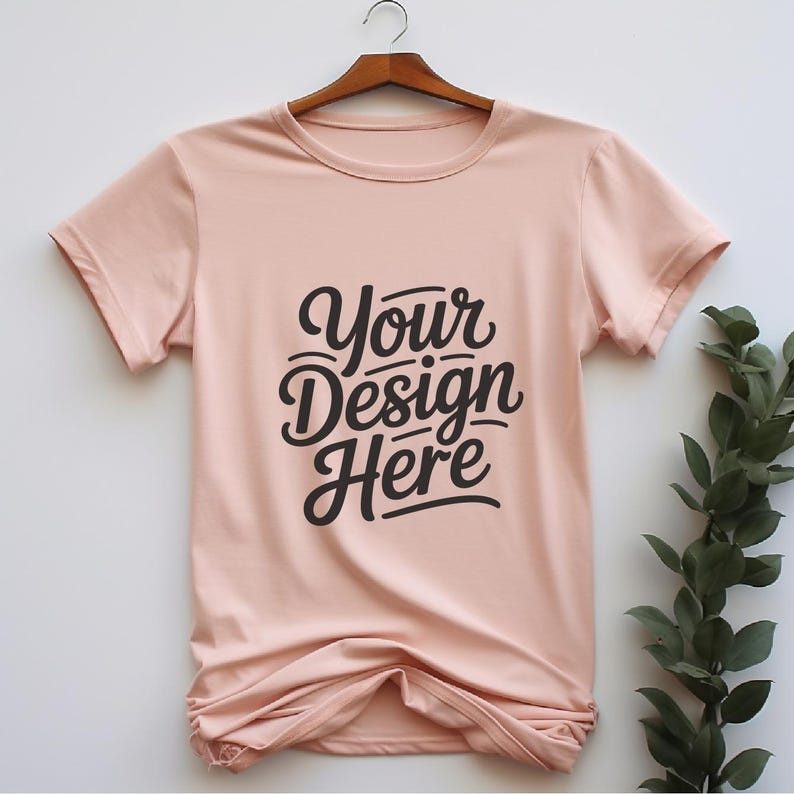 K&ouml;nnte beinhalten: Ein hellrosa T-Shirt mit kurzen &Auml;rmeln und Rundhalsausschnitt. Das Shirt hat den Text "Your Design Here" in Schwarz auf der Vorderseite aufgedruckt.