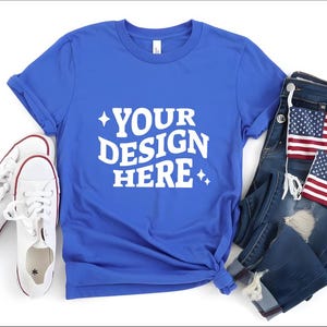 May include: A royal blue t-shirt with the text "YOUR DESIGN HERE" in white, paired with white sneakers, distressed denim jeans, and two American flag patches. The t-shirt is knotted at the bottom.