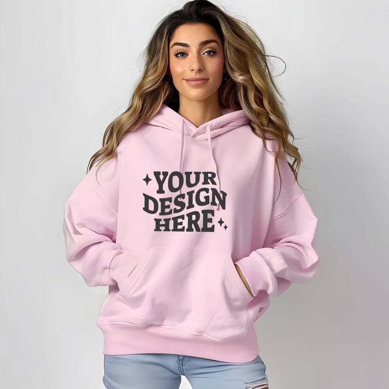 Pu&ograve; includere: Una felpa con cappuccio rosa con una grande grafica nera che dice "YOUR DESIGN HERE" in un font retr&ograve;.