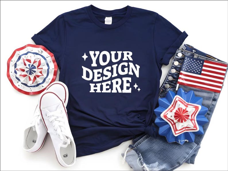 May include: Navy blue t-shirt with the text "YOUR DESIGN HERE", paired with white sneakers, denim shorts, and patriotic decorations. The ensemble includes a red, white, and blue paper fan and a star-shaped pin.