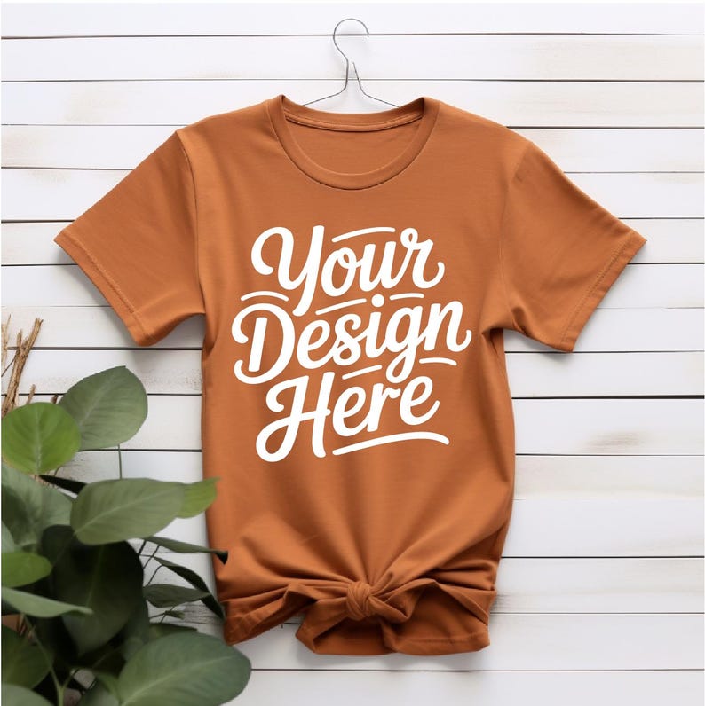 K&ouml;nnte beinhalten: Ein rostfarbenes T-Shirt mit kurzen &Auml;rmeln und einem Rundhalsausschnitt. Das Shirt hat den Text "Your Design Here" in Wei&szlig; auf der Vorderseite aufgedruckt.