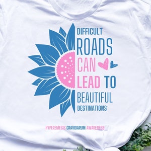 May include: White t-shirt featuring a blue sunflower graphic and the text "Difficult roads can lead to beautiful destinations".