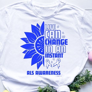 May include: White t-shirt with a blue sunflower graphic and the text "Life can change in an instant ALS Awareness".