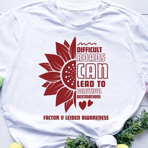 May include: White t-shirt with a red sunflower graphic and the text "Difficult roads can lead to beautiful destinations. Factor V Leiden Awareness".