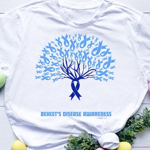 May include: White t-shirt with a blue ribbon tree design and the text "Behcet's Disease Awareness".