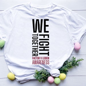May include: White t-shirt with the words "WE FIGHT TOGETHER" in black vertical text. Below, in red, is "FACTOR V LEIDEN AWARENESS". The shirt is styled with Easter eggs and greenery.