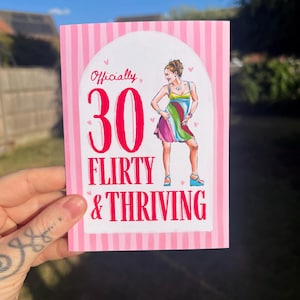 Peut inclure: Une carte de vœux rectangulaire avec une bordure à rayures verticales roses et blanches. Le centre présente une arche blanche avec le texte Officially 30 FLIRTY & THRIVING en rose et rouge, et une illustration d'une personne en robe colorée.
