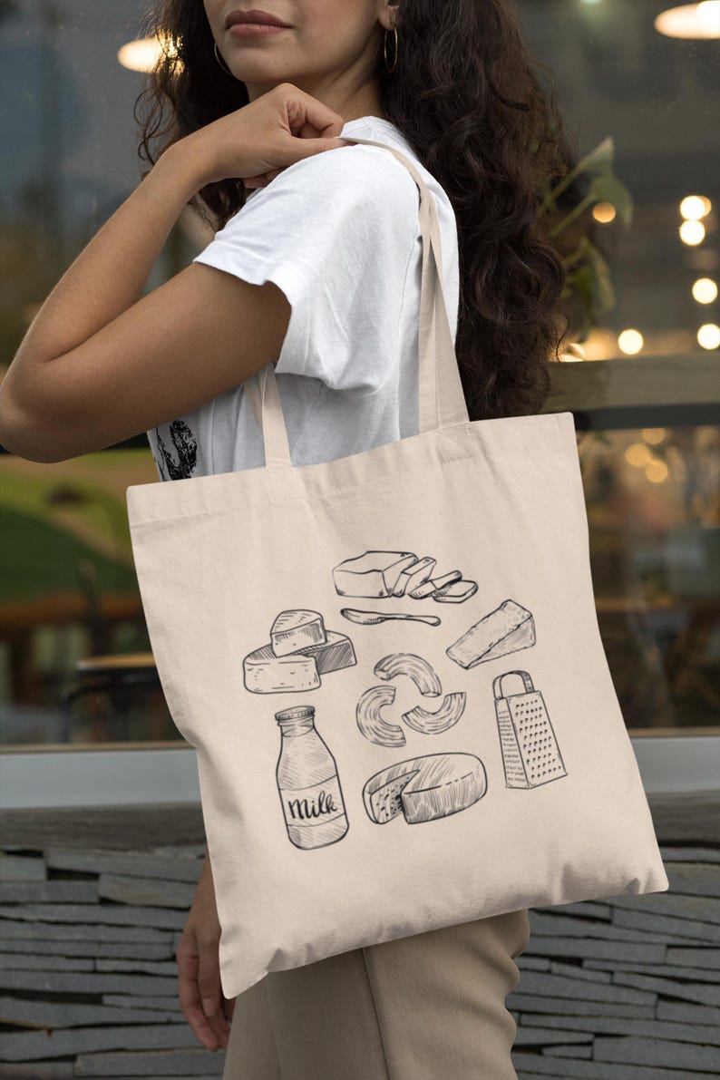 Op de afbeelding: Een beige canvas draagtas met een zwarte lijntekening van diverse zuivelproducten, waaronder een melkfles met het woord Milk erop, een kaasrasp, verschillende soorten kaas, een blok boter en een botermes.