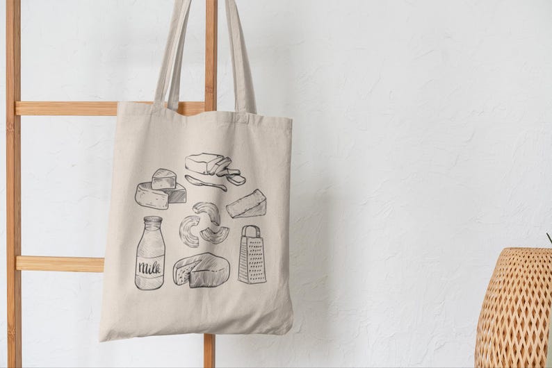 Op de afbeelding: Een beige canvas draagtas met een zwarte lijntekening van diverse zuivelproducten, waaronder een melkfles met het woord Milk erop, een kaasrasp en verschillende soorten kaasstukken die op de voorzijde van de tas zijn afgebeeld.