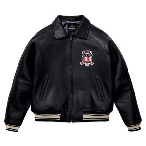 May include: Black leather jacket with a classic collar and a zip-up front. Features a patch on the chest with the text "AVIREX" and an American flag design. The jacket has a ribbed hem and cuffs with cream and beige stripes.