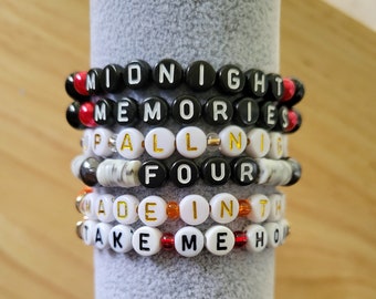 May include: Five beaded bracelets with different colored beads and letters spelling out the phrases "Midnight Memories", "Fall in Four", "Made in the", and "Take Me Home".