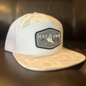 May include: White camouflage trucker hat with a black and grey patch that says "Hat Down Waterfowl" and features a flying duck.