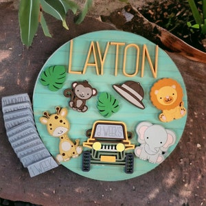 May include: A light blue wooden growth chart with a jungle theme. The chart features a giraffe, monkey, lion, elephant, and a jeep. The name "LAYTON" is written in yellow letters at the top of the chart. There are also numbers for months and weeks.