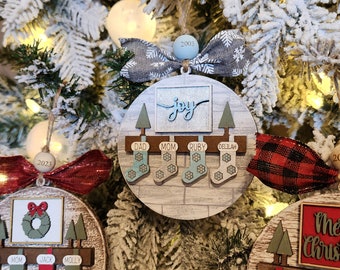 May include: Christmas tree ornaments with family names and stockings. One ornament says "joy" and has the names "Dad, Mom, Ruby, Delilah". Another says "Mom, Jack, Molly". The tree is decorated with lights and snow.