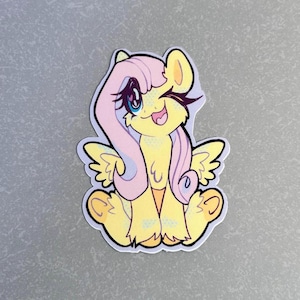 May include: A yellow and pink cartoon pony with a pink mane and wings, winking and sticking out its tongue. The pony is sitting down with its legs crossed.