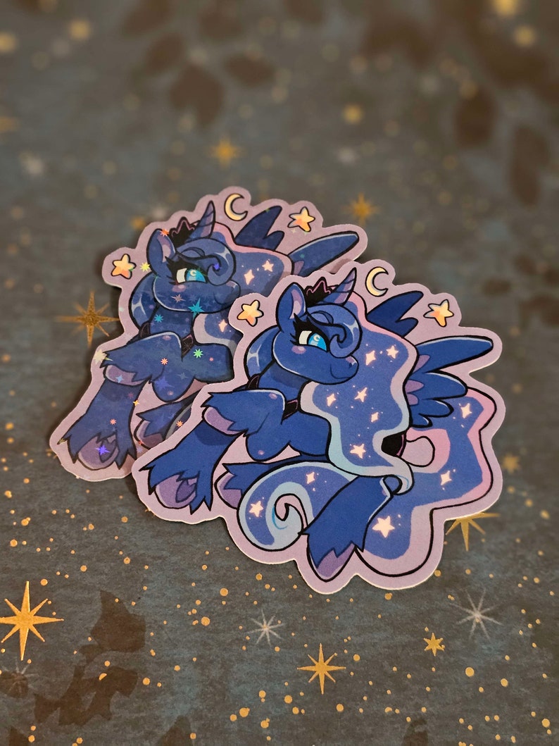 Op de afbeelding: Twee iriserende stickers van Prinses Luna van My Little Pony. De stickers zijn op een donkerblauwe achtergrond met gouden sterren. De stickers zijn paars en blauw met een halve maan en sterren.