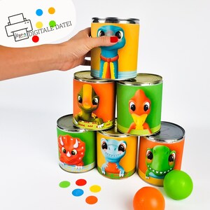 May include: A stack of six colorful cans with dinosaur illustrations. The cans are arranged in a pyramid shape. The top can features a blue dinosaur with a red tie. The other cans feature green, orange, and red dinosaurs. There are also colorful dots and a green ball in the image.