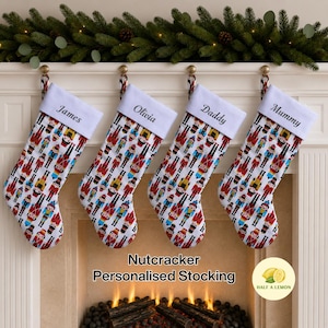 May include: Four Christmas stockings featuring a repeating nutcracker pattern on a white background. Each stocking has a white cuff embroidered with the names James, Olivia, Daddy, and Mummy. The stockings hang from a white fireplace mantel.