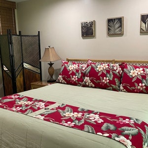 May include: A king-sized bed with a green duvet and a red floral bed runner. The headboard is made of woven wicker and there are three framed pictures on the wall behind the bed.