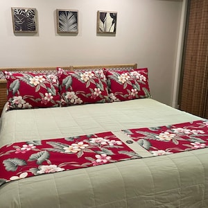May include: A king-sized bed with a green duvet and a red floral patterned bed runner. The bed has a wicker headboard and three red floral patterned pillows.