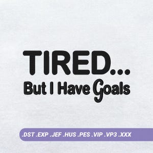 May include: An embroidery design on a white fabric background featuring the black text TIRED... But I Have Goals. Below the text is a light purple horizontal bar containing the file formats .DST .EXP .JEF .HUS .PES .VIP .VP3 .XXX in white text.