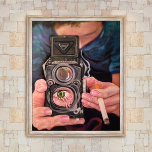 May include: A close-up of a person holding a vintage Rolleiflex camera. The camera is pointed at the viewer, and the lens is focused on a green eye with a small, fleshy hand inside. The person is holding a cigarette in their other hand.