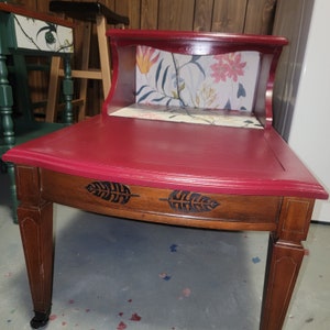 May include: A red end table with a floral patterned shelf and a dark wood base with leaf designs. The table has a curved top and a single shelf.