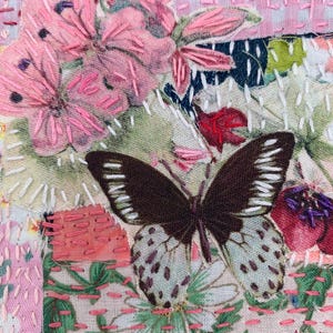 May include: Close-up of a textile art piece featuring a butterfly with brown and white wings, surrounded by pink embroidered flowers and stitching. The background includes floral patterns and patches of fabric.