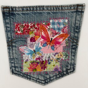 May include: A denim pocket with a patchwork design featuring two butterflies. The butterflies have orange, pink, and blue wings. The patchwork includes floral patterns in red, pink, and blue.