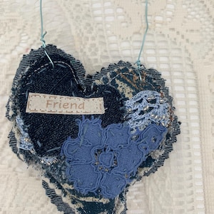 May include: A handmade denim heart pendant with a blue lace flower and the word "Friend" on a small fabric tag. The heart is embellished with silver beads and a blue wire hanger. A blue bead dangles from the bottom.