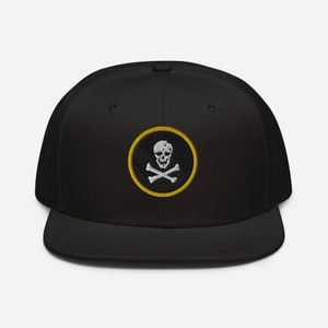 May include: Black and yellow embroidered skull and crossbones patch on a black baseball cap.