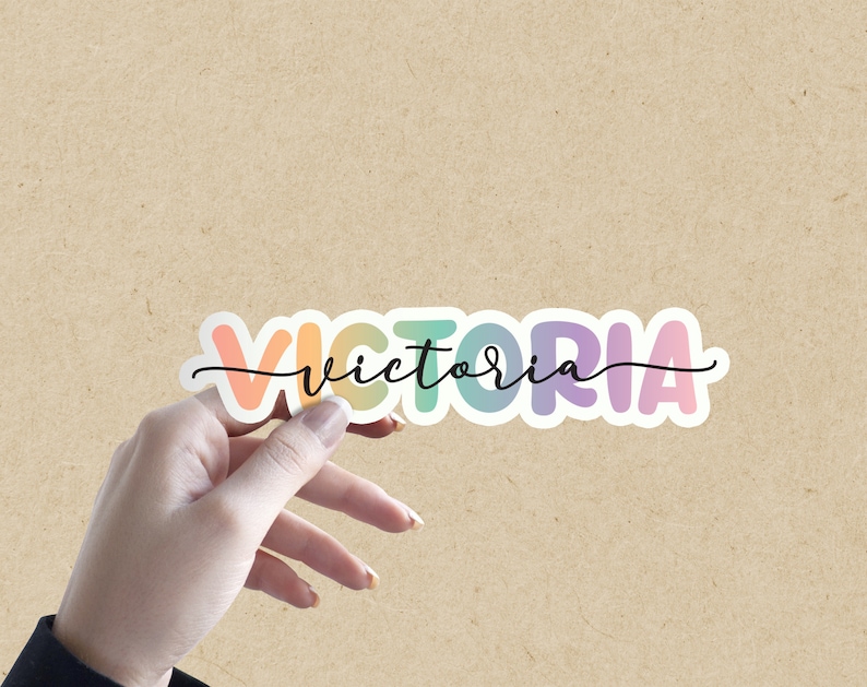 May include: A colorful sticker with the name "VICTORIA" written in a rainbow gradient font. The sticker is on a brown background.