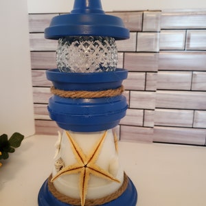 May include: Blue and white lighthouse-shaped decorative object with a starfish and seashells. The lighthouse is made from terracotta pots and has a glass globe on top.
