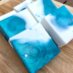 May include: Five bars of handmade soap with a teal and white swirl design. The soap is on a wooden surface.